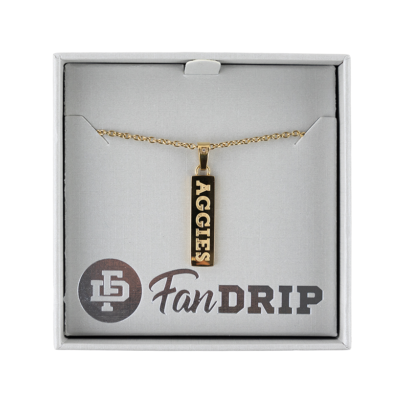 A gold necklace with a gold rectangular pendant. On the pendant, 'AGGIES' is spelled in gold block lettering. 