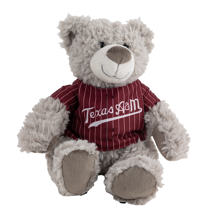 A light grey teddy bear wearing a maroon and white striped baseball jersey with 'Texas A&M' written across the chest