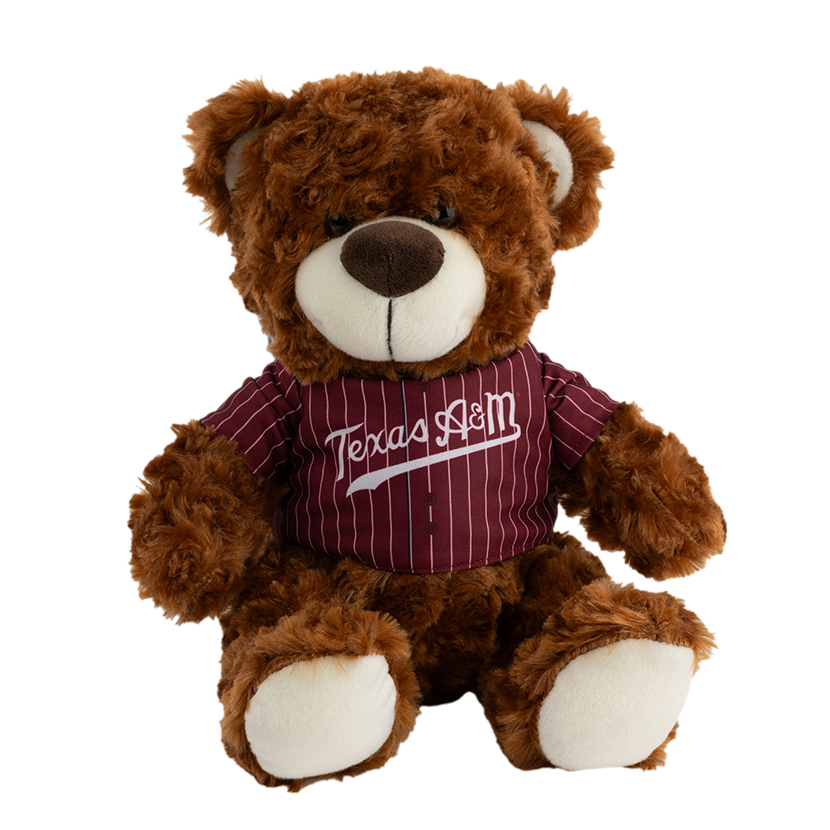 A light brown teddy bear wearing a maroon and white striped baseball jersey with 'Texas A&M' written across the chest