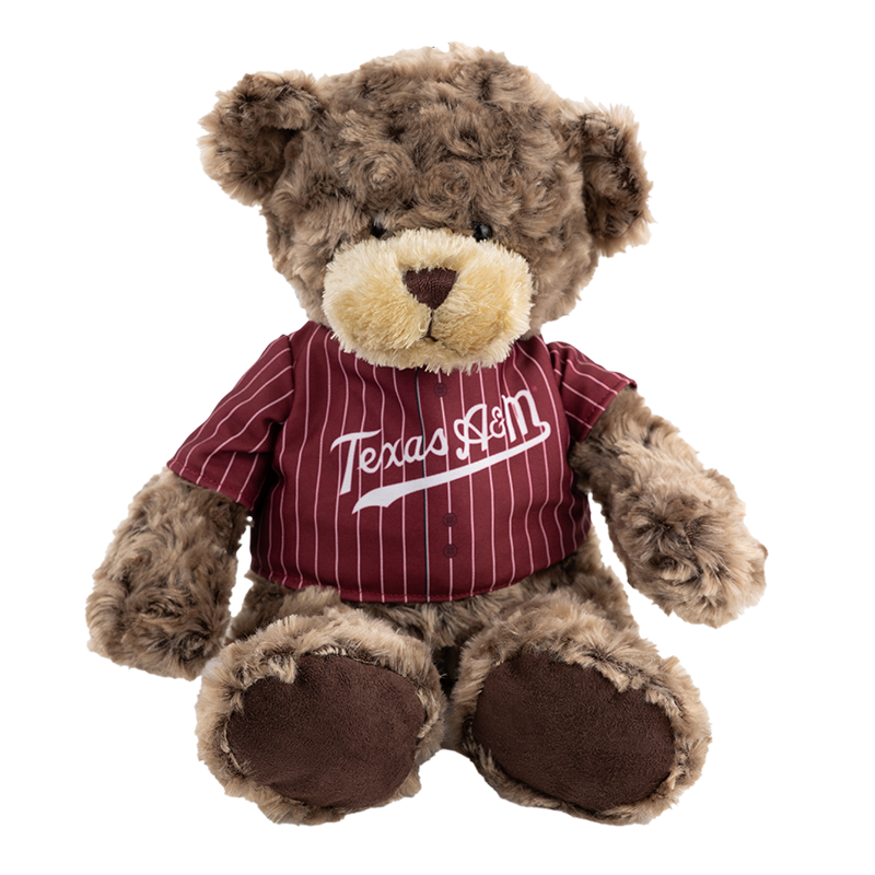 A dark brown teddy bear that is wearing a maroon and white striped baseball jersey with 'Texas A&M' written across the chest